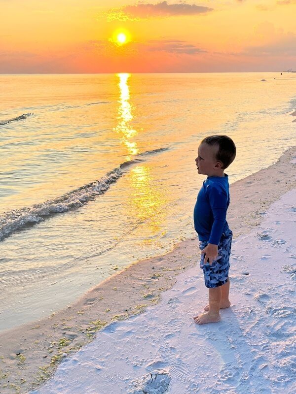 Child waving to strangers on the golden hour on the beach, spreading joy with a simple gesture