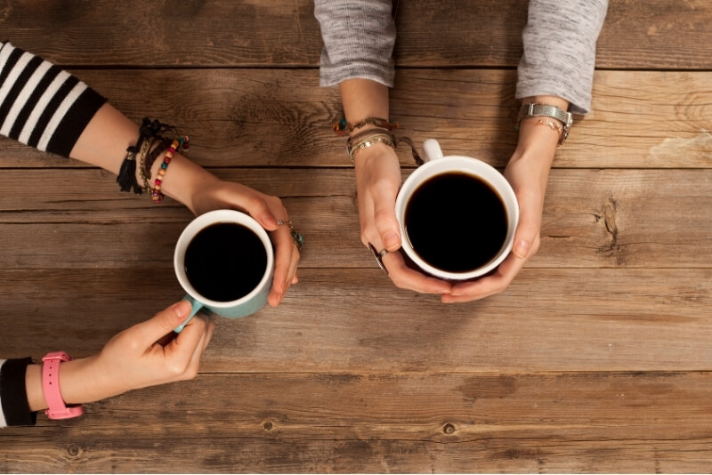 Two friends sitting together over coffee, listening and talking in a relaxed, supportive conversation.
